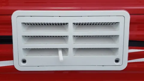 3D-printed louvered refrigerator sidewall vent cover installed on the side of a camper van